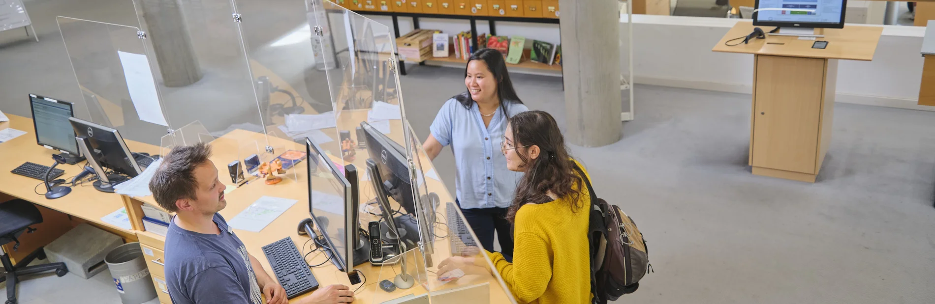 Mitarbeiter an der Theke berät zwei Studentinnen