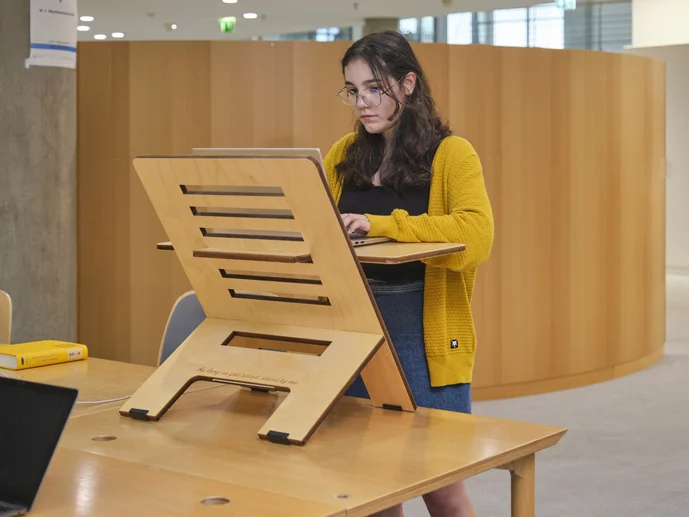 Studentin steht vor einem Stehpult und arbeitet am Laptop, der auf dem Stehpult liegt in der Zentralbibliothek