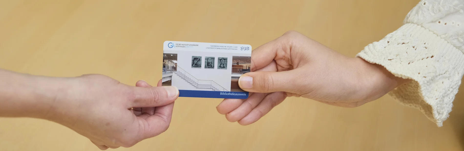 Zwei Hände reichen sich einen Bibliotheksausweis