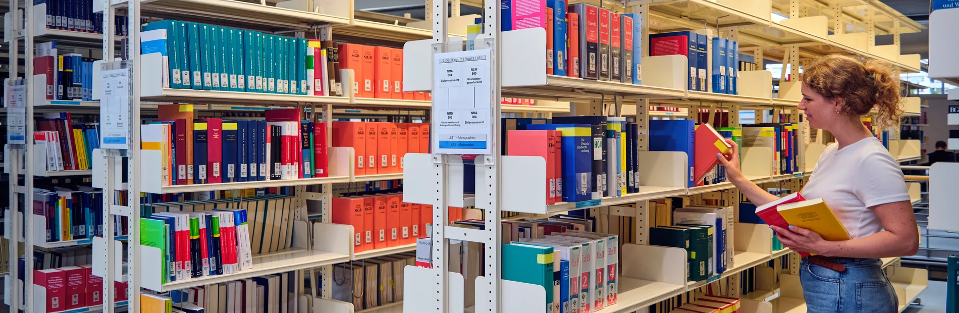Studentin zieht ein Buch aus einem Regal im Lesesaal der Zentralbibliothek