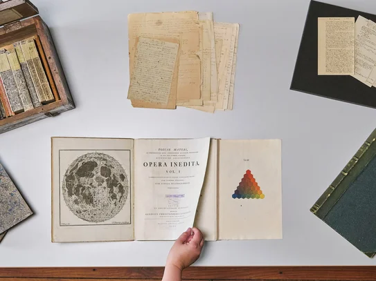 Historische Sammlungen der SUB Göttingen Tisch mit historischen Büchern und Archivmaterialien, eine Hand blättert in einem Buch