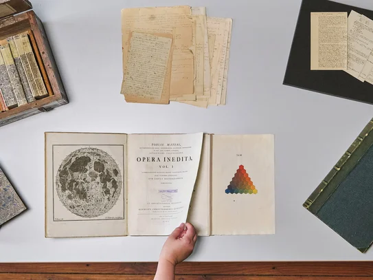 Historische Sammlungen der SUB Göttingen Tisch mit historischen Büchern und Archivmaterialien, eine Hand blättert in einem Buch