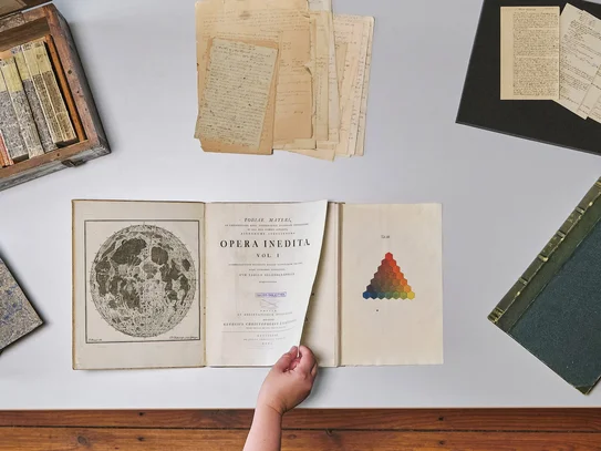 Historische Sammlungen der SUB Göttingen Tisch mit historischen Büchern und Archivmaterialien, eine Hand blättert in einem Buch