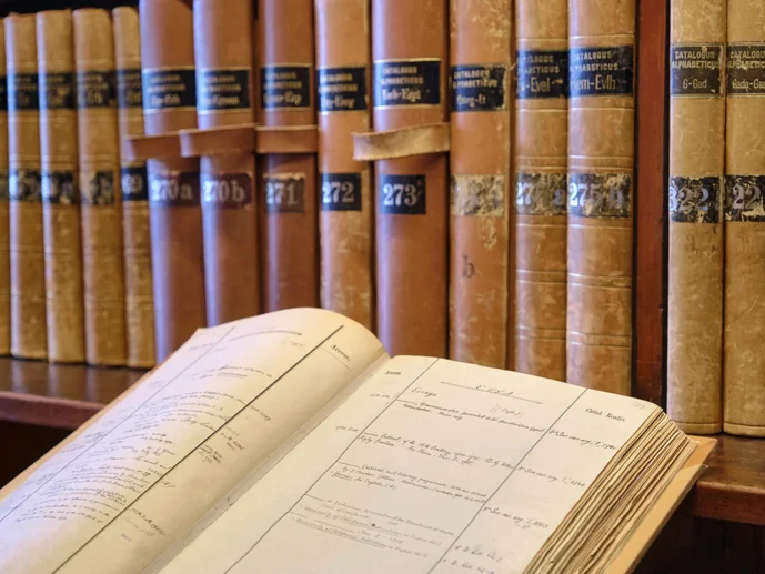 Historische Bibliothekskataloge aus Göttingen Im Hintergrund Bibliothekskataloge auf einem Regal, im linken vorderen Bereich ein aufgeschlagener Bibliothekskatalog