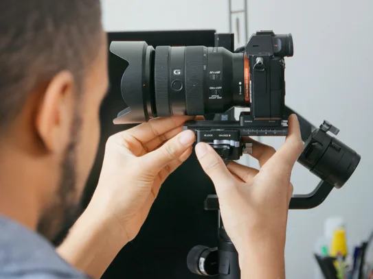 Person justiert eine spiegellose Kamera mit großem Objektiv auf einem Stativ im Innenraum