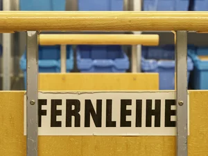 Blaue Kisten im Hintergrund, im Vordergrund ein Bücherwagen mit der Aufschrift Fernleihe