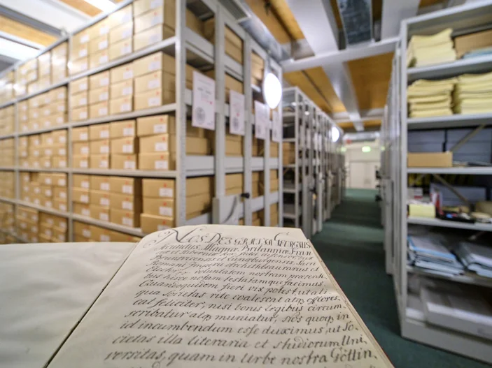 Gründungsurkunde der Universität Göttingen im Magazin Gründungsurkunde der Universität Göttingen im Vordergrund, dahinter Regale mit Archivalien