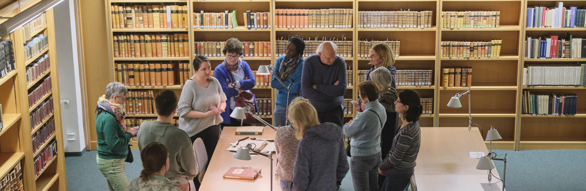 Ein Vortrag vor historischen Büchern, dem eine Gruppe von Menschen aufmerksam folgt