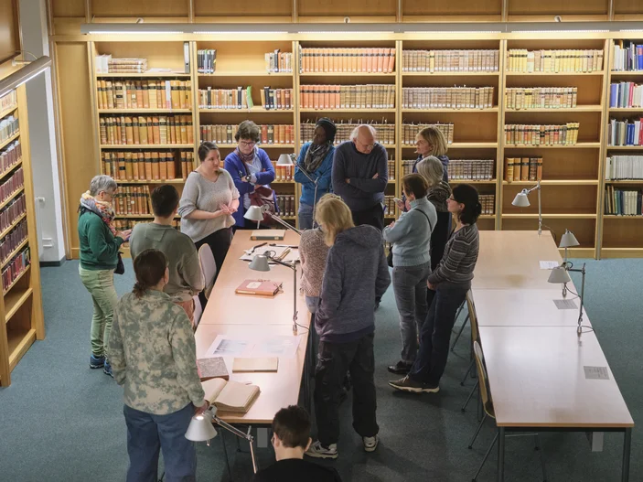 Einführung in die Benutzung von Altbeständen Ein Vortrag vor historischen Büchern, dem eine Gruppe von Menschen aufmerksam folgt