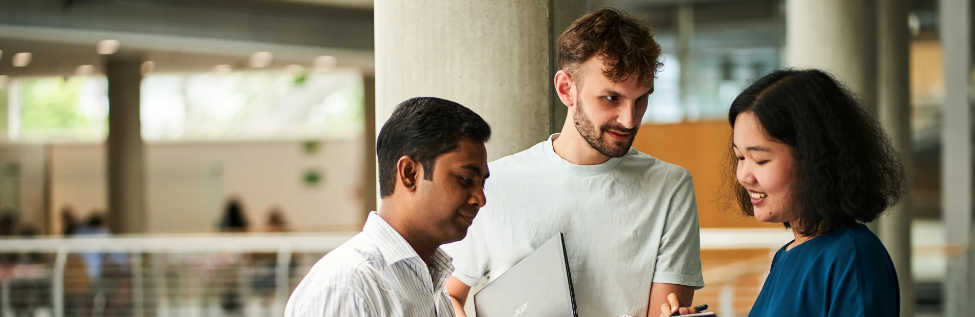 Drei Personen in der Zentralbibliothek. Eine Person hält ein Tablet, eine andere ein Laptop. Die dritte Person hat ein Smartphone in der Hand.