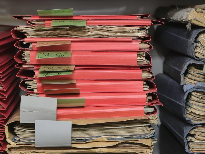 Blick ins Akademiemagazin Drei Stapel mit roten und blauen Mappen, die historische Materialien enthalten