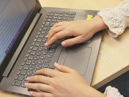Eine Person arbeitet am Laptop. Auf dem Bildschirm ist eine Textdatei geöffnet.