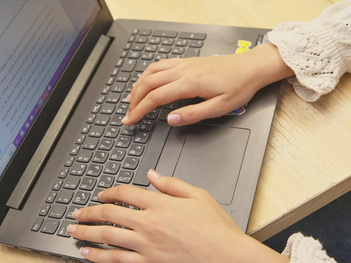 Eine Person arbeitet am Laptop. Auf dem Bildschirm ist eine Textdatei geöffnet.