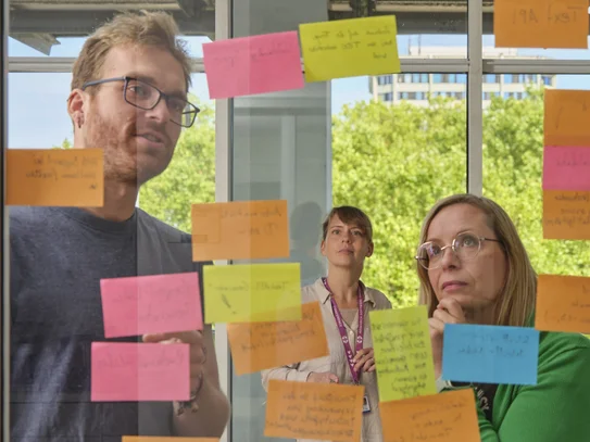 Drei Personen schauen auf Post-its und beraten sich