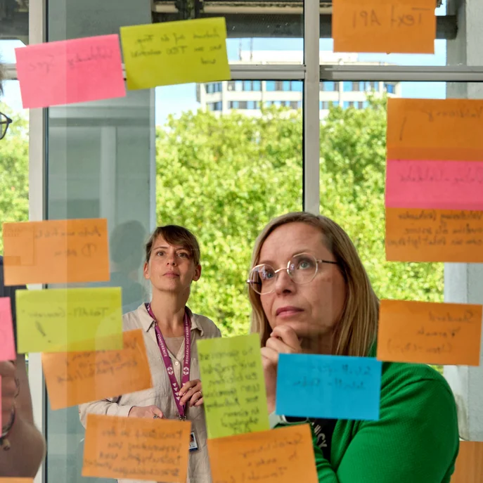 Personen stehen vor einer Glaswand mit beschriebenen Notizzetteln und beraten sich.