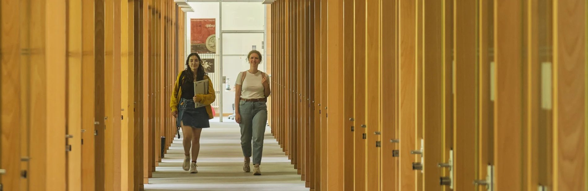 Zwei Studentinnen gehen einen Gang zwischen Arbeitskabinen in der Zentralbibliothek entlang