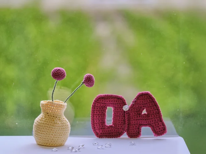 Gehäkeltes OA-Symbol und Blumenwase auf grünen Hintergrund