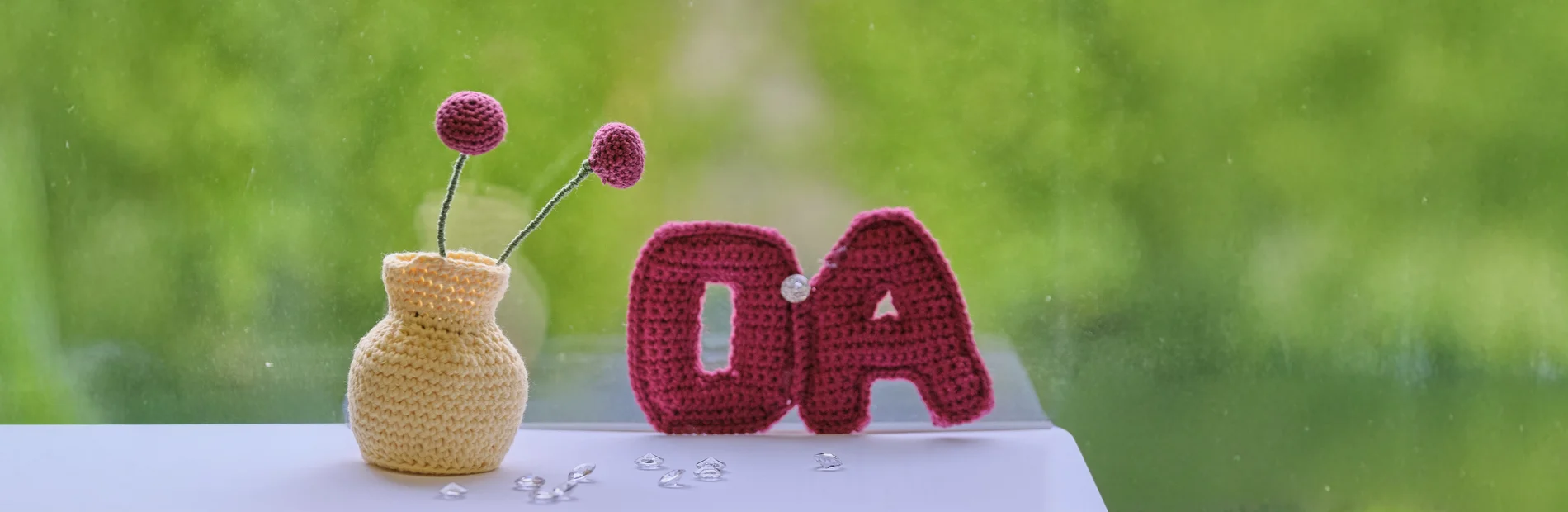 Gehäkeltes OA-Symbol und Blumenwase auf grünen Hintergrund