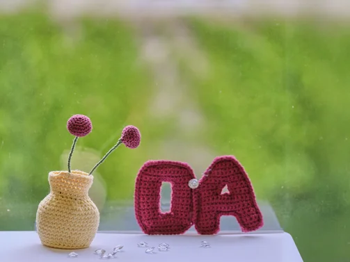 Gehäkeltes OA-Symbol und Blumenwase auf grünen Hintergrund